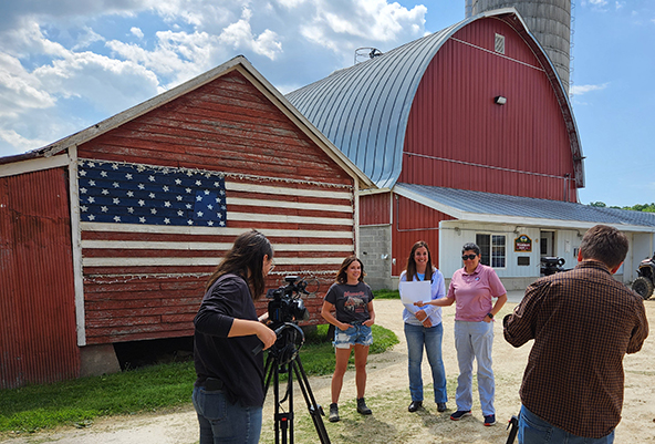 cameramen pointing cameras at three people standing in front of a barn